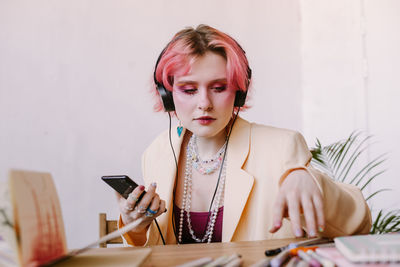 Creative young woman using smartphone , listen to music at table with scetchbook and painting 