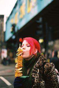 Woman eating from skewer on street in city