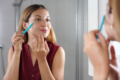 Brazilian girl shaving her face by razor at home. beautiful young woman using razor on bathroom.