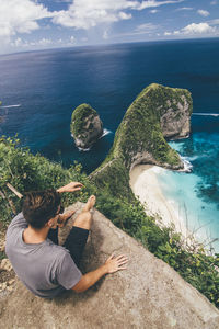 Rear view of man on rock by sea against sky