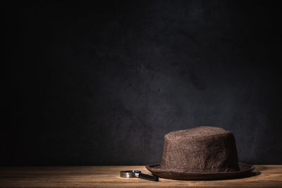 Hat and magnifying glass against black background on table