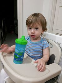 Portrait of girl sitting on high chair with water bottle at home