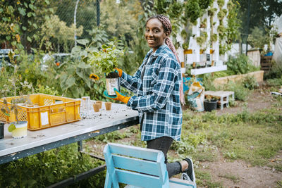 Portrait of smiling female farmer with potted plant in community garden