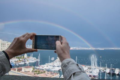 Midsection of person photographing rainbow in city