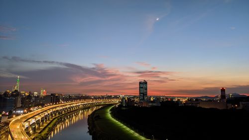 Illuminated buildings in city against sky during sunset