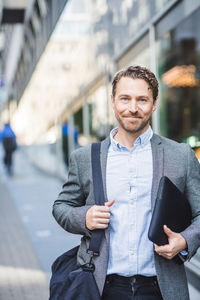 Portrait of smiling mature entrepreneur with bag standing outdoors