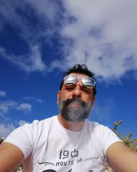 Low angle view of mature man wearing sunglasses while smoking against sky