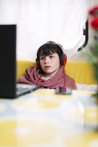 Front view of teen sitting on sofa with headphones looking laptop