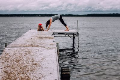 Young woman with daughter doing yoga on pier over lake