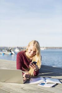 Happy high school girl using mobile phone on pier