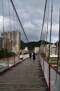 People walking on footbridge against sky