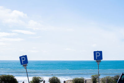 Information sign by sea against sky