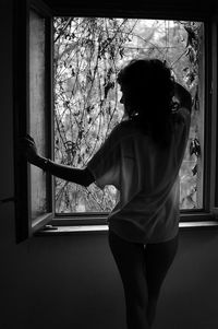 Rear view of sensual woman standing by window at home