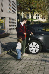 Man with daughter charging electric car while standing at station