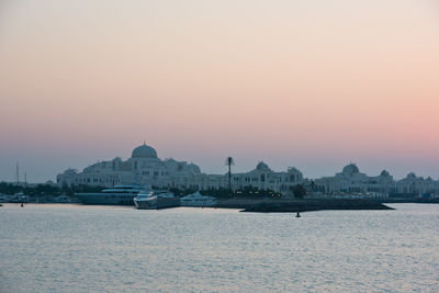 Sea by buildings against sky during sunset