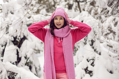 Woman enjoy in pink clothes a jacket a knitted scarf and a hat stands in a snowy forest in winter