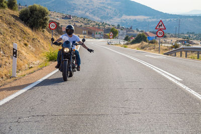 Young man gesturing while riding motorcycle on road