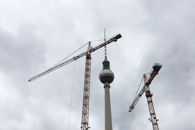 Low angle view of fernsehturm and cranes against sky