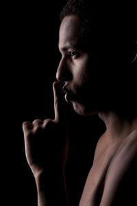 Shirtless man shushing against black background