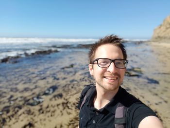 Portrait of smiling young man at beach against sky
