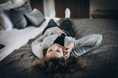 Happy smiling teenager girl talking by phone lying on her back on the bed