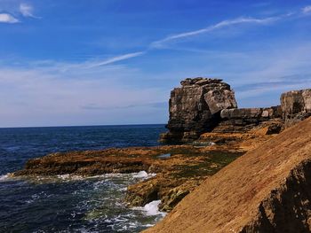 Scenic view of cliff by sea against blue sky