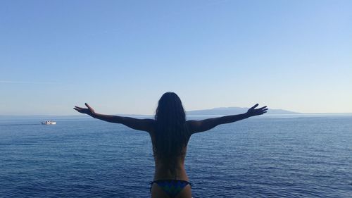 Rear view of woman standing by sea against clear sky