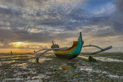 Fishing boats moored on beach against sky during sunset