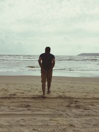 Rear view of man walking at beach against sky