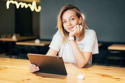 Portrait of young woman using phone while sitting on table