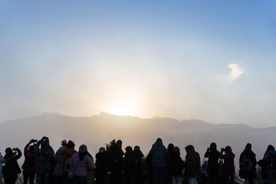 People looking at mountains against sky