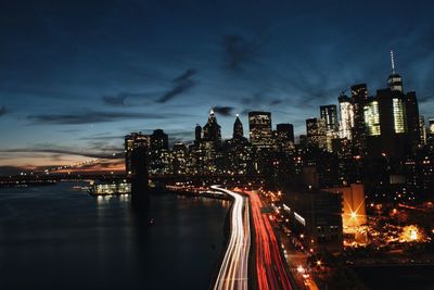 Light trails on street in manhattan by river against sky