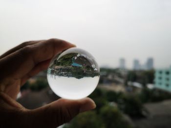 Close-up of hand holding crystal ball against sky