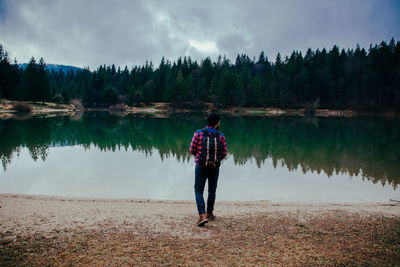 Rear view of man standing by lake against sky