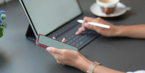 Cropped hands of woman using digital tablet while holding mobile phone