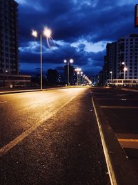 Road by illuminated buildings against sky at night