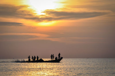 Silhouette people in sea against sky during sunset