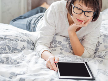 Woman in glasses are lying in bed with tablet. she is touching screen. 