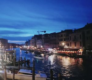 Illuminated buildings by canal against sky at night