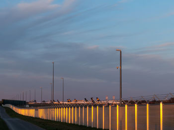 Street lights by bridge against sky at dusk