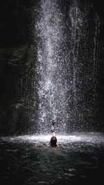 Rear view of man surfing in waterfall