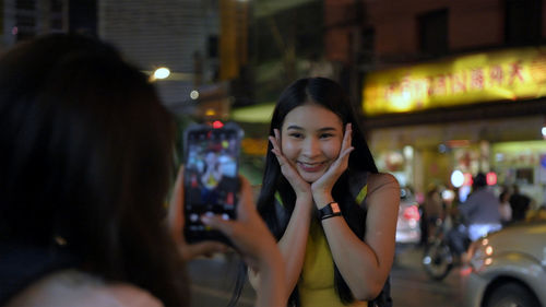 Portrait of smiling young woman using phone on city at night