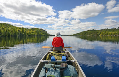 Rear view of man sitting on boat in lake against sky