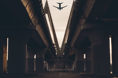 Low angle view of airplane flying over bridge in city