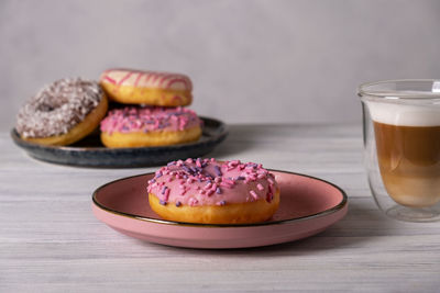 Glazed donuts on plates and coffee latte or cappuccino with milk foam in a heat-resistant glass cup. 