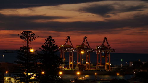 Cranes at harbor against cloudy sky