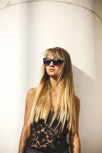 Young woman wearing sunglasses against wall