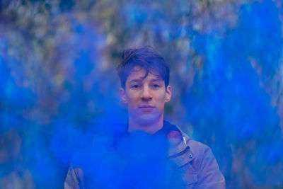 Portrait of young man holding distress flare while standing in forest