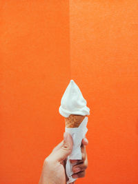 Close-up of hand holding ice cream against orange wall