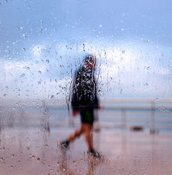 Rear view of man walking on wet window in rainy season